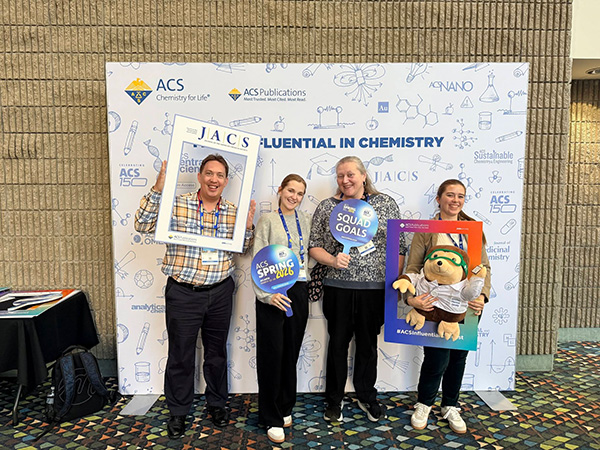 Four people posing in front of an American Chemical Society (ACS) backdrop at the Spring 2026 conference.